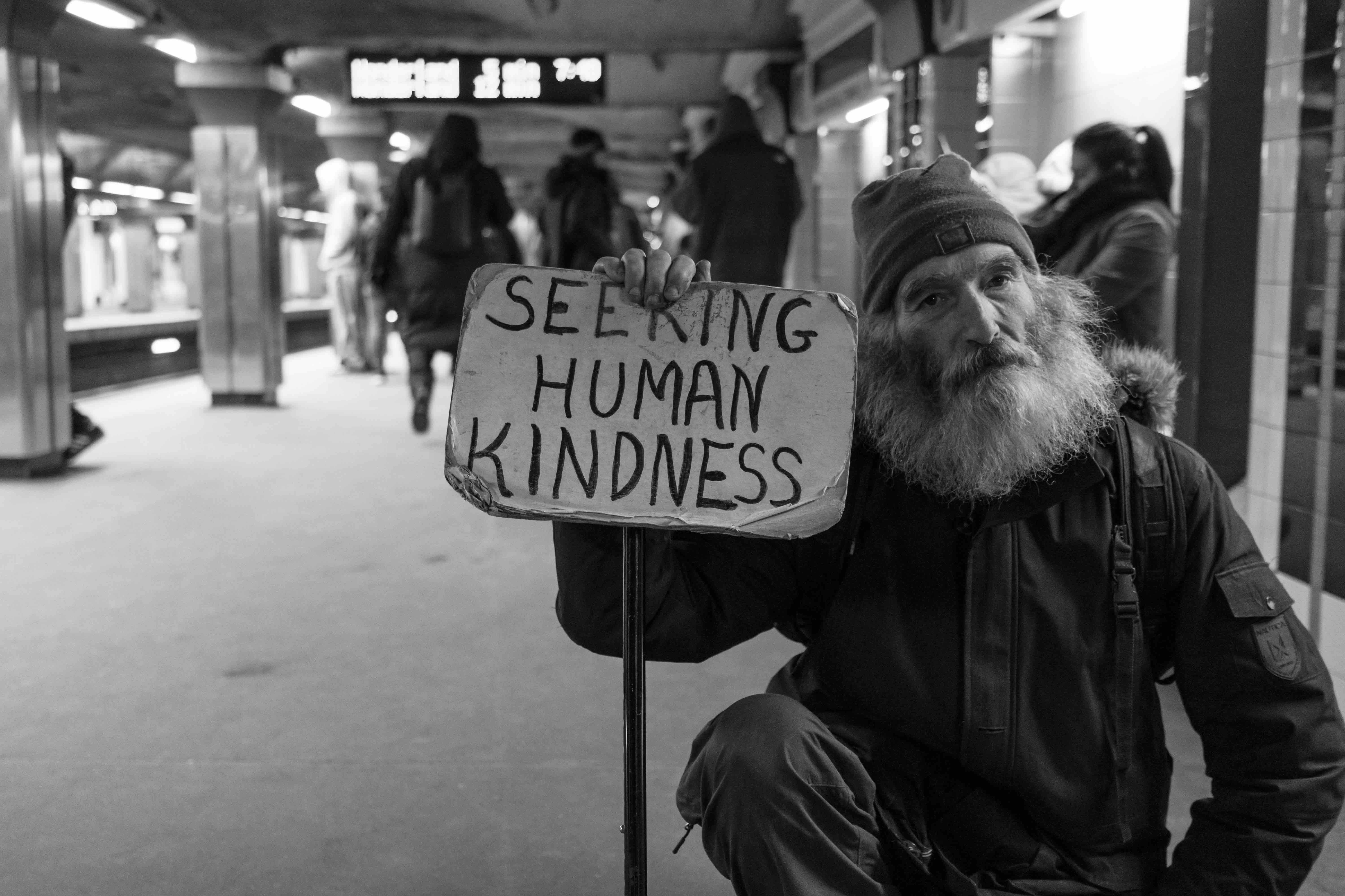 Scruffy man holding a human kindness sign